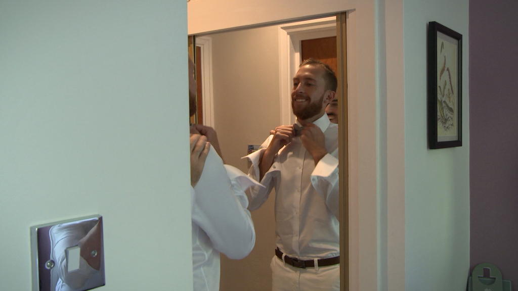 the groom gets some help from his best man to straighten his bow tie on his white shirt