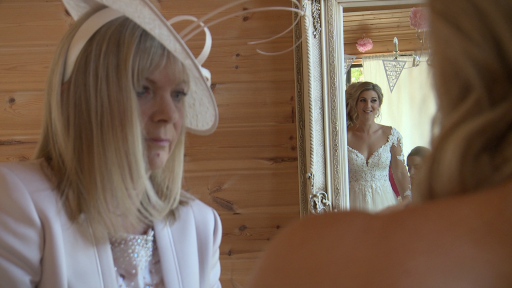 mother of the bride checks her daughter in her wedding dress as she smiles at herself in the mirror in styal lodges bridal room