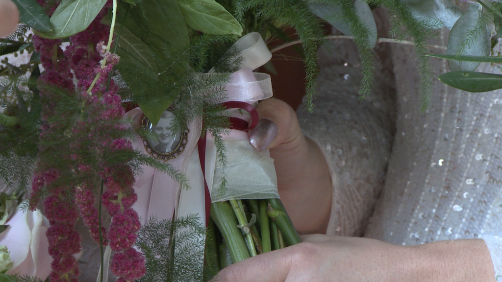 a close up shot of a vintage style open locket with an old black and white photo of the bride's grandma inside. tied with a purple ribbon on to her hand tied rustic bridal bouquet