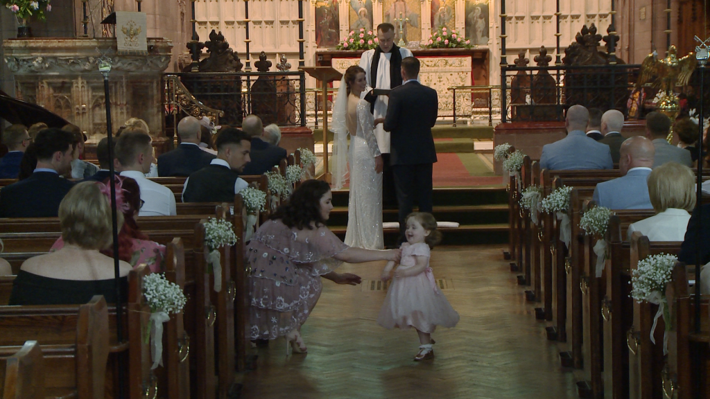 the videographer films a flower girl running down the aisle as her mum tried to catch her during a wedding ceremony at St Peters in Woolton