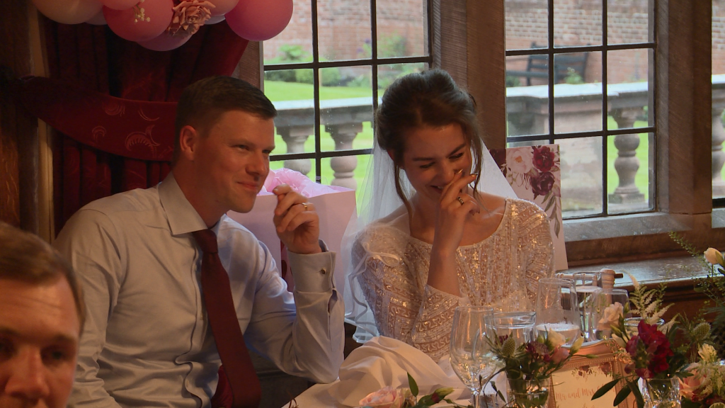The groom smirks as the bride laughs during the best mans speech at inglewood manor