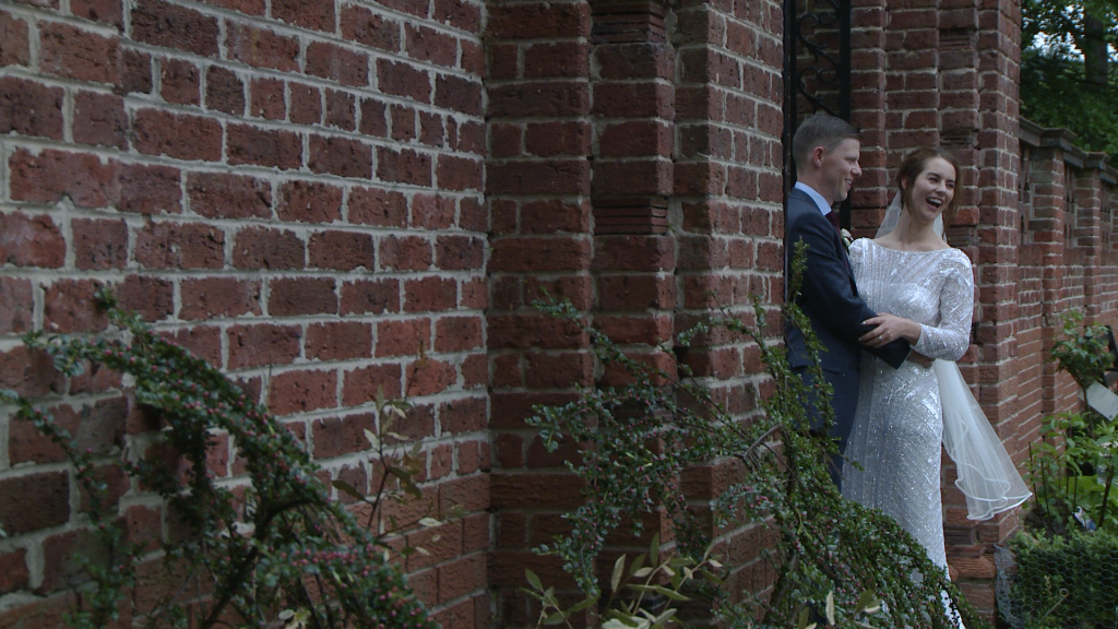 the bride and groom laugh with the wedding photographer as she takes photos by the garden gate in Inglewood manor