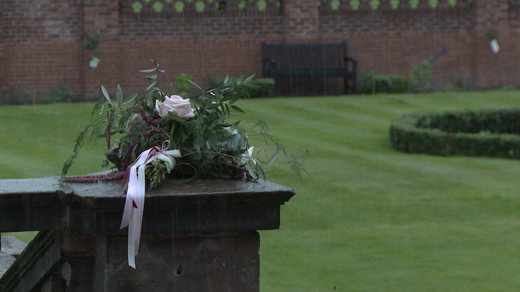 a large oversized rustic bridal bouquet lays on a wall as the rain bounces off it at a rainy wedding at inglewood manor