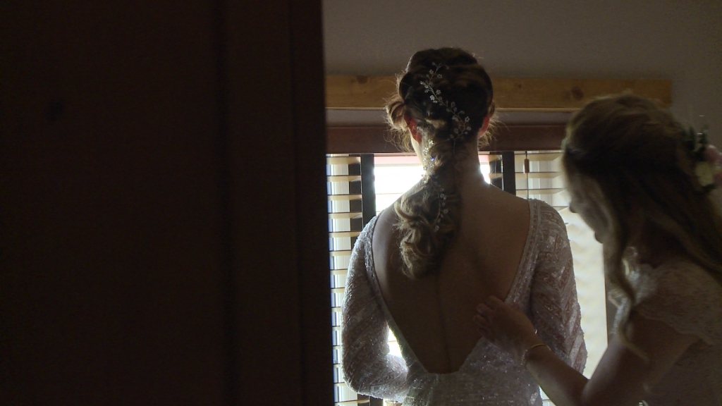 a bridesmaid does the final checks of the brides Eliza Jane Howell beaded wedding dress