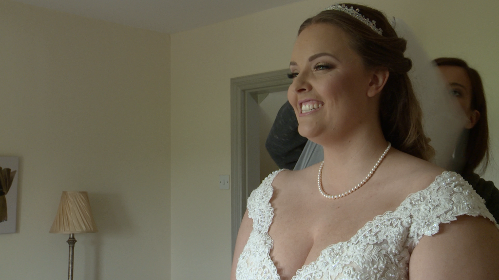 a bride beams with a huge smile as she has the wedding veil put in
