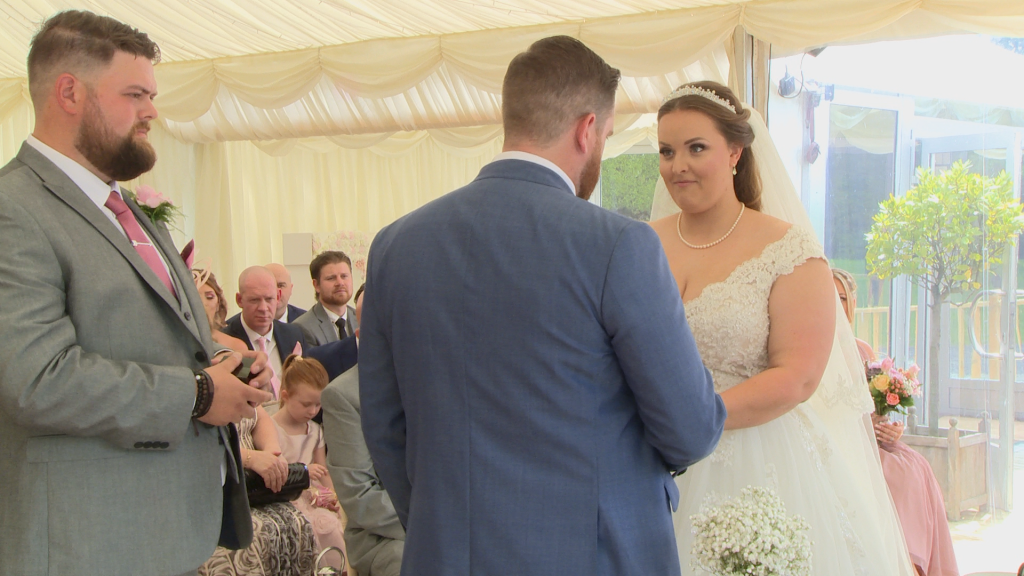 the bride looks up and smiles at her groom as he puts the ring on her finger during their wedding ceremony