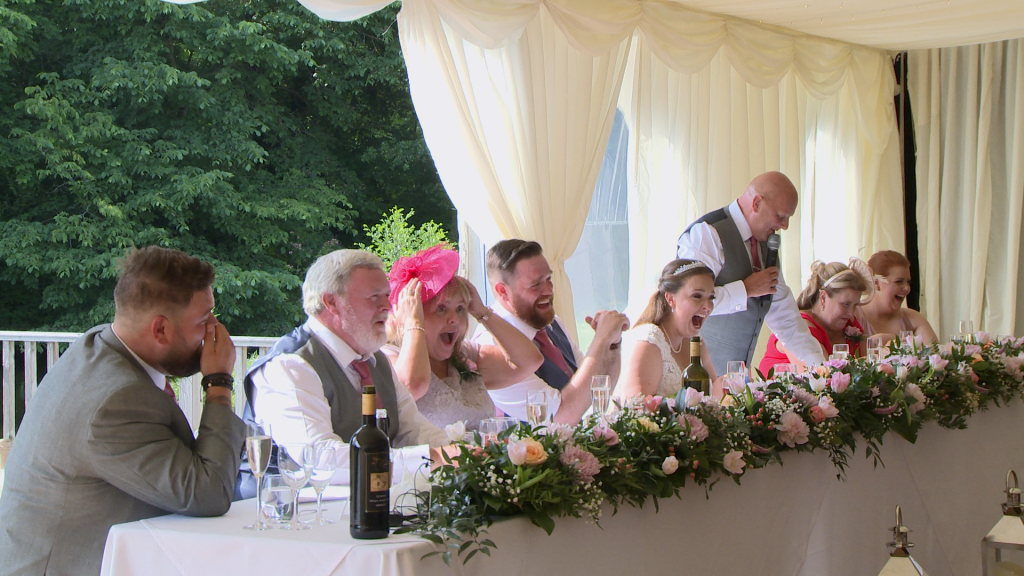 the brides dad says something funny about the bride and everyone is laughing and shocked he could be so funny