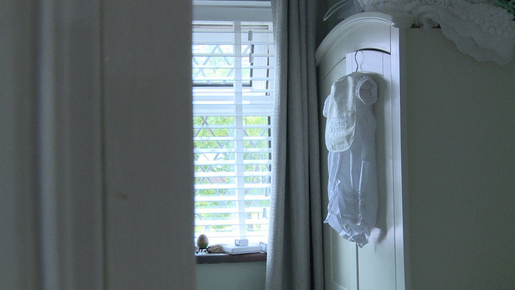a traditional white silk boys christening gown hangs on a baby wardrobe in a nursery at their home near Warrington