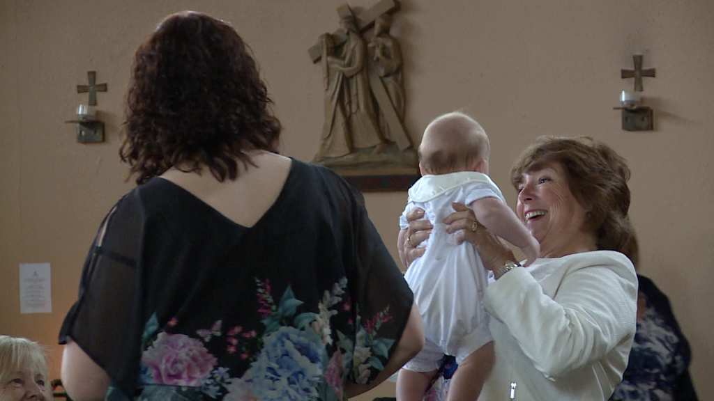 a grandma holds her grandson up high with a huge smile on her face before his christening in burtonwood