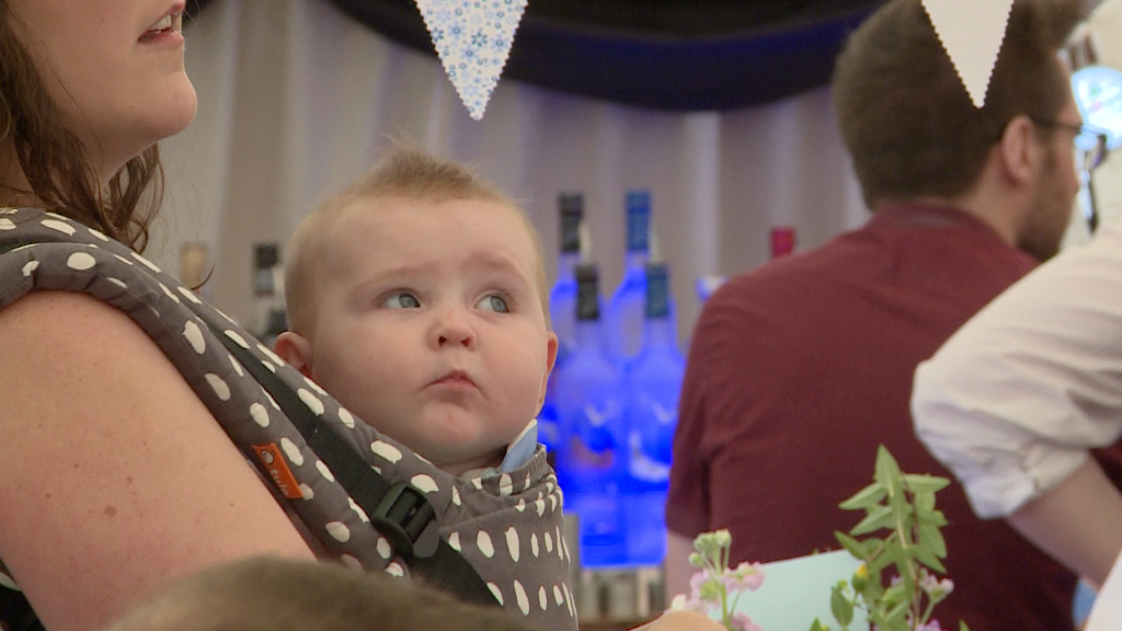 a cute baby girl looks up in a carrier on her mum at Alder Root Golf Club marquee for a christening party