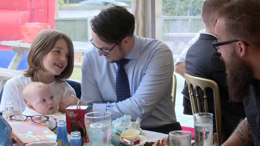a young boy holds baby as his Dad sits next to him at a christening party at Alder Root Golf Club in Warrington
