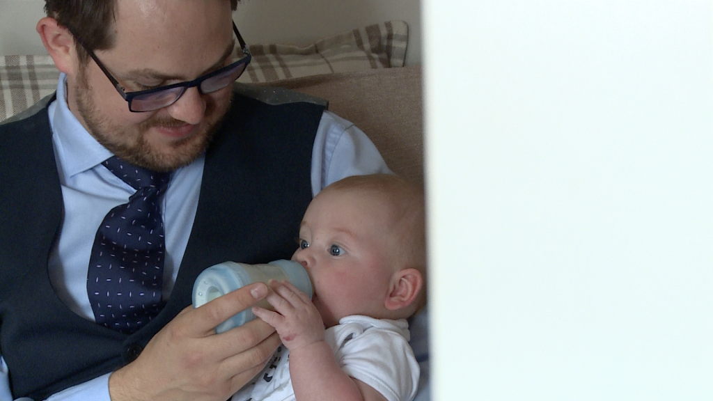 family video still dad smiles as he feeds his baby boy a bottle of milk at home