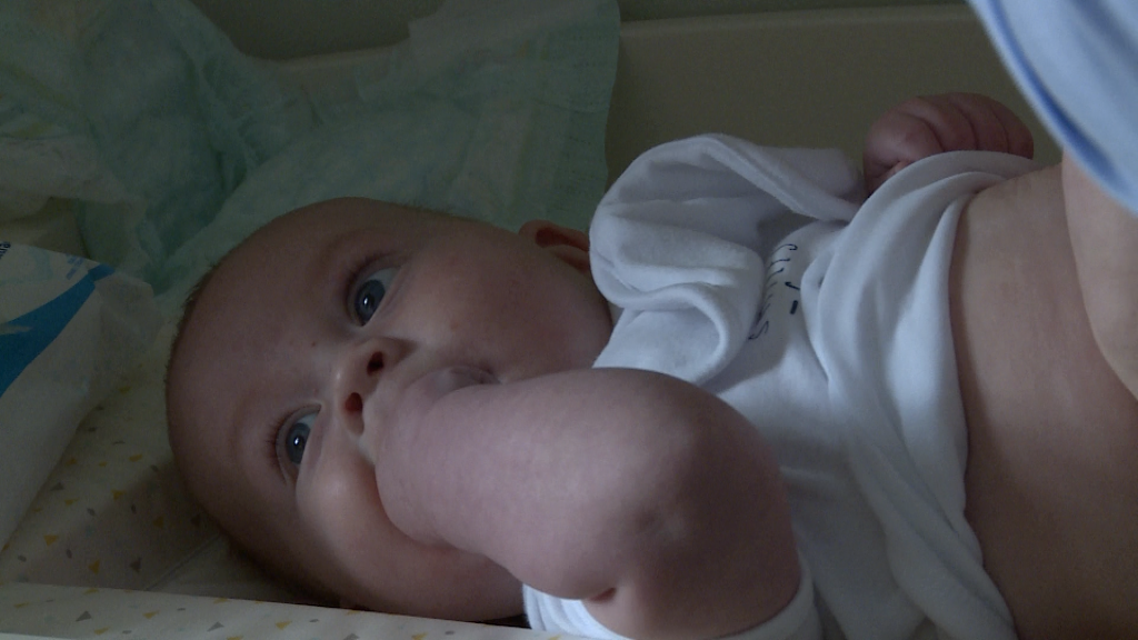 a baby boy gets his bum changed wearing a white vest and sucking his hands