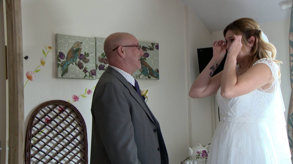 the bride wipes her tears away after her Dad sees her for the first time in her wedding dress captured for the wedding video