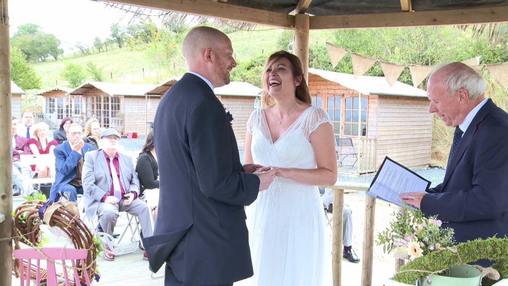a bride and groom laugh out loud as they get the wedding rings stuck on his finger during a wedding ceremony at abel's harp in Shrewsbury