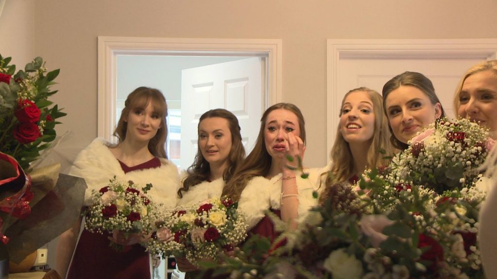 a close up of bridesmaids wearing long red dresses and faux fur shrugs holding red rose and gypsy grass bouquets getting emotional and crying when they see the bride for the first time at a home in preston