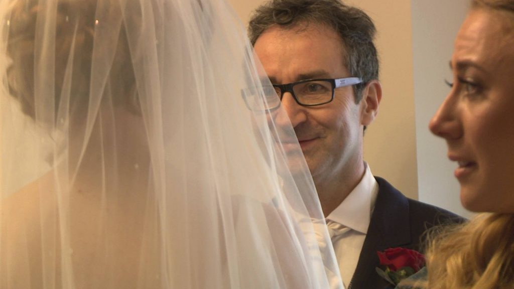a close up from the wedding video of a proud dad smiling at his daughter the bride