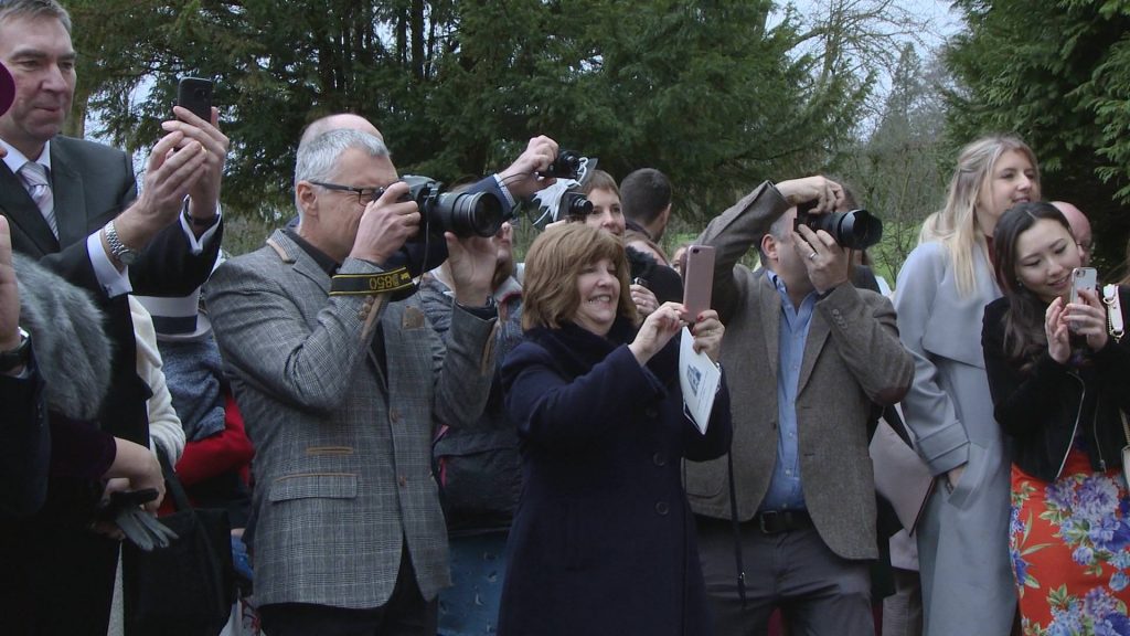a row of guests and the professional wedding photographer taking photos outside Broughton Church