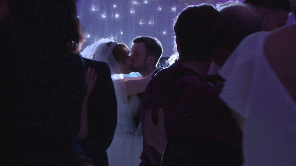 a close up video still of the groom kissing the brides cheek through a crowed dancefloor at the villa wrea green