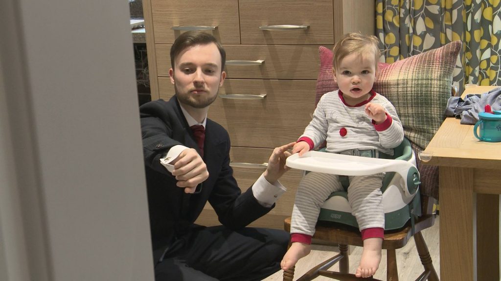 a groom shows off his wedding watch as a little page boy sits in his high chair and stares at the wedding videographer