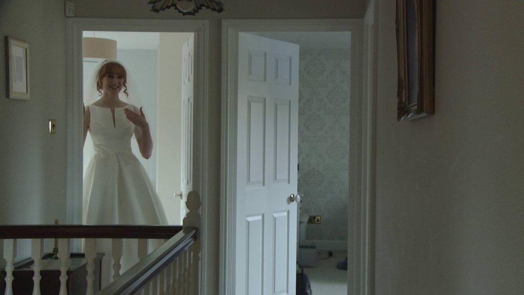 a bride stands in a doorway and fans herself as she takes a minute before she walks down the stairs to show her bridesmaids her wedding dress