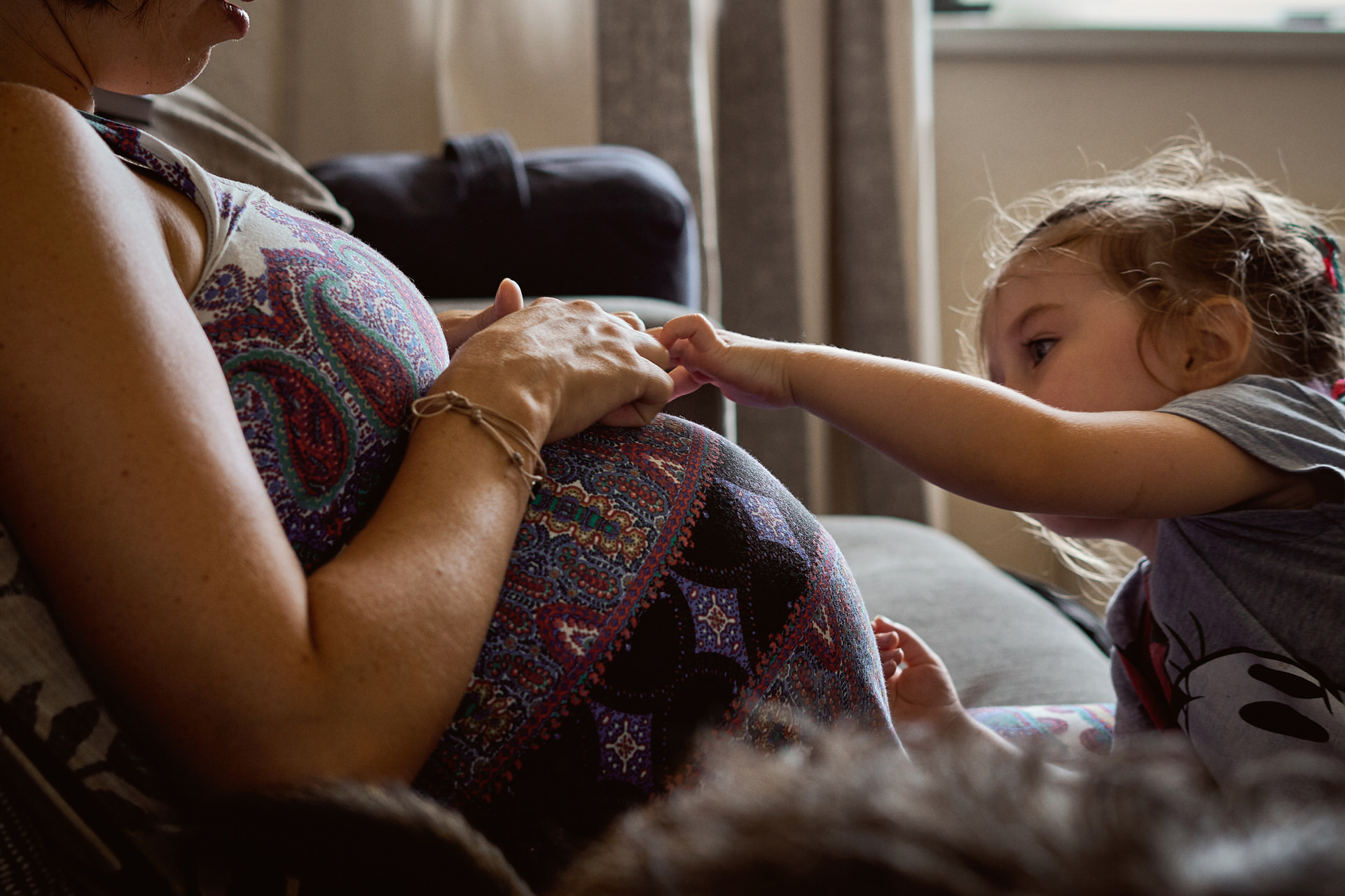 photo of little girl reaching out to touch a baby bump