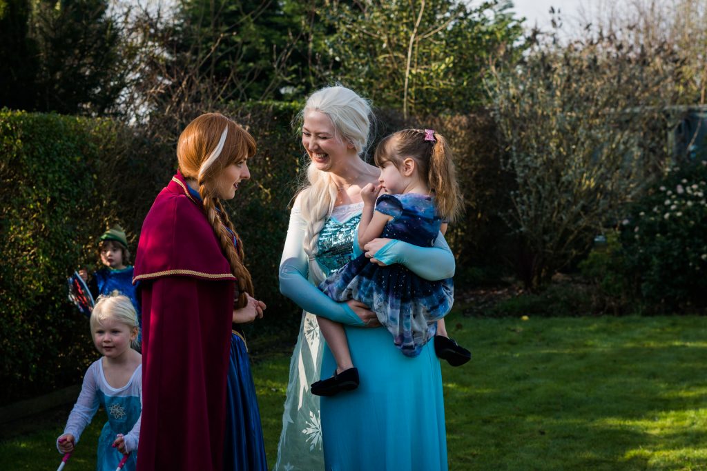 a photograph of a birthday party. elsa holds the birthday girl as they chat with Anna from Frozen during her 4th birthday party celebrations at home in Burscough
