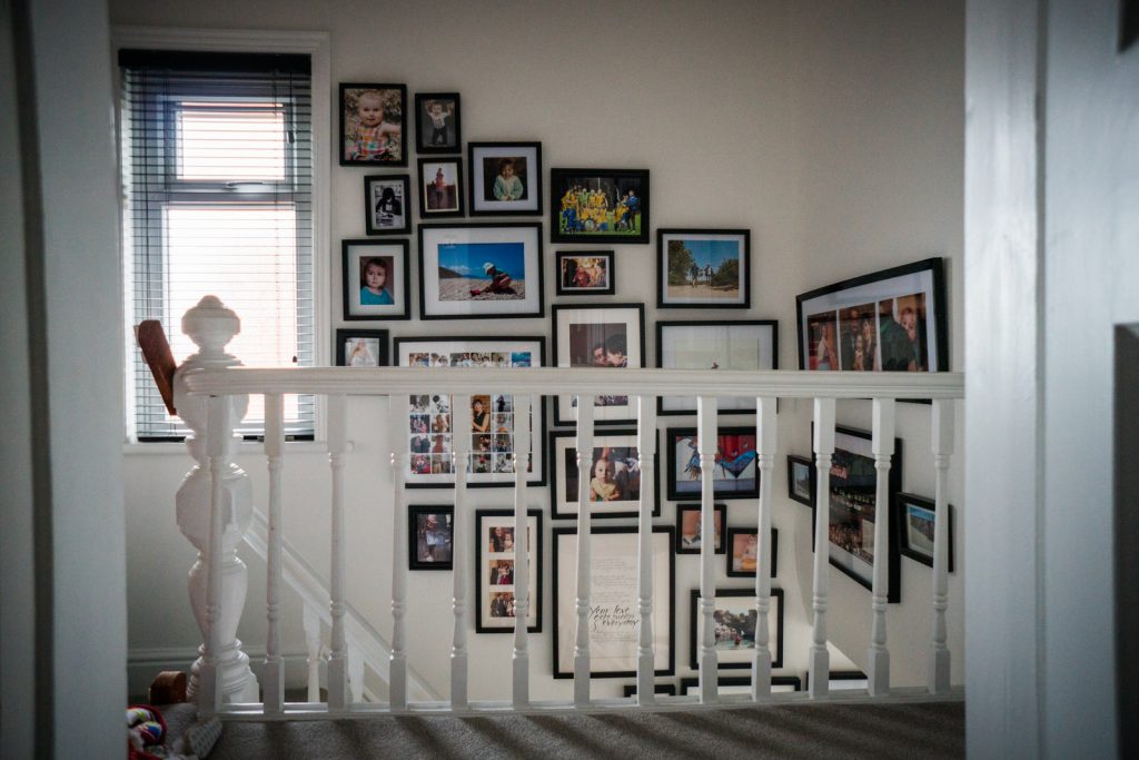 you can see the start of a fun family photo wall creeping up the stairs using black chunky photo frames on a white wall in a family home in Lancashire