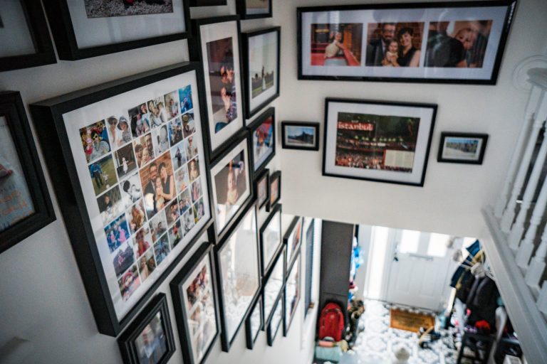 looking down the stairs to the front door we can see a colelction of chunky black picture frames with a variety of personal and professional family photographs framed in a feature photo wall at a home in Lancashire