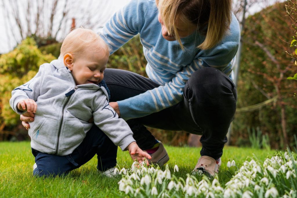 a little girl leans to touch the new snowdrops growing in the garden with her Mum during a relaxed family photo and video shoot