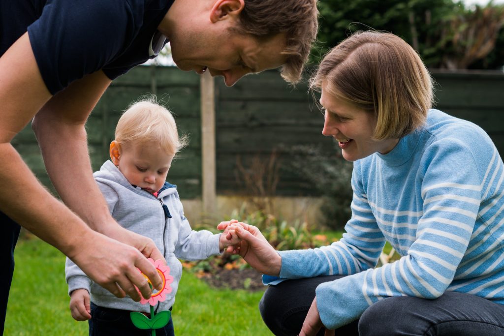 a girl holds her mums hand as she crouches down with dad to chat during a family photography shoot in their garden in Hale near Manchester