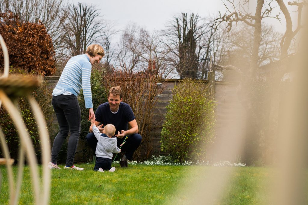 a photo taken at distance through a garden chair of a young family playing in the garden in hale