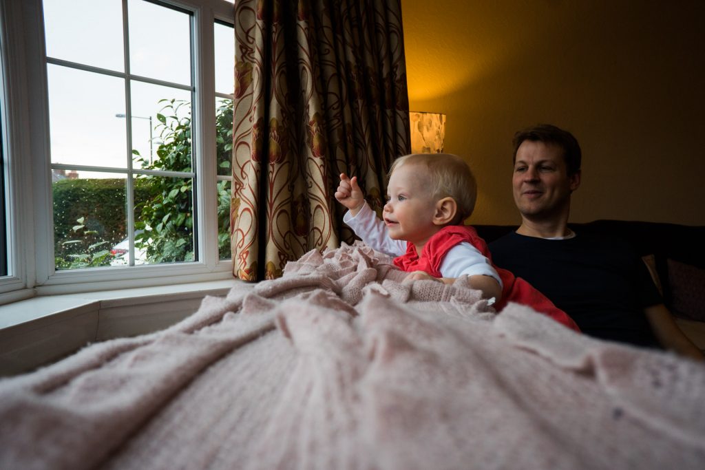 a little girl leans on the sofa and points at the rain outside the window during a family photo shoot at their home in hale