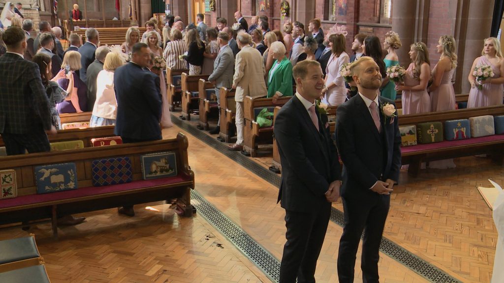 a still from the wedding video of the groom looking up nervously as he waits for the bride to walk down the aisle at Oxton St Saviours Wirral
