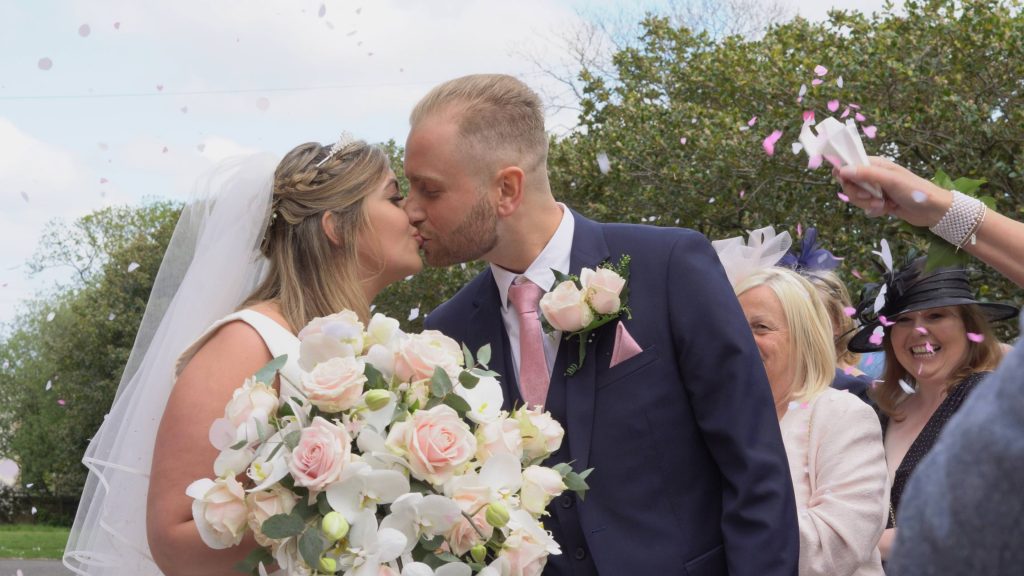 a still from the wedding video of the pink cofetti shot outside church the bride holds an oversized blush pink and white boquet