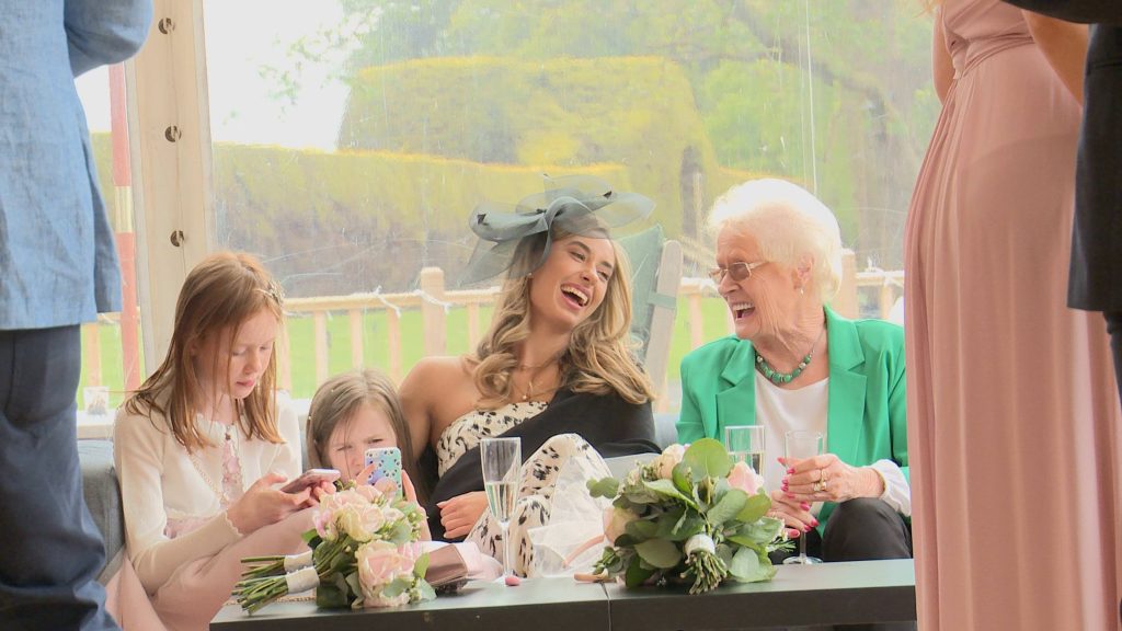 a few guests sit on a sofa at the lakeside marquee at thornton manor laughing and enjoying the sunshine during a wedding reception