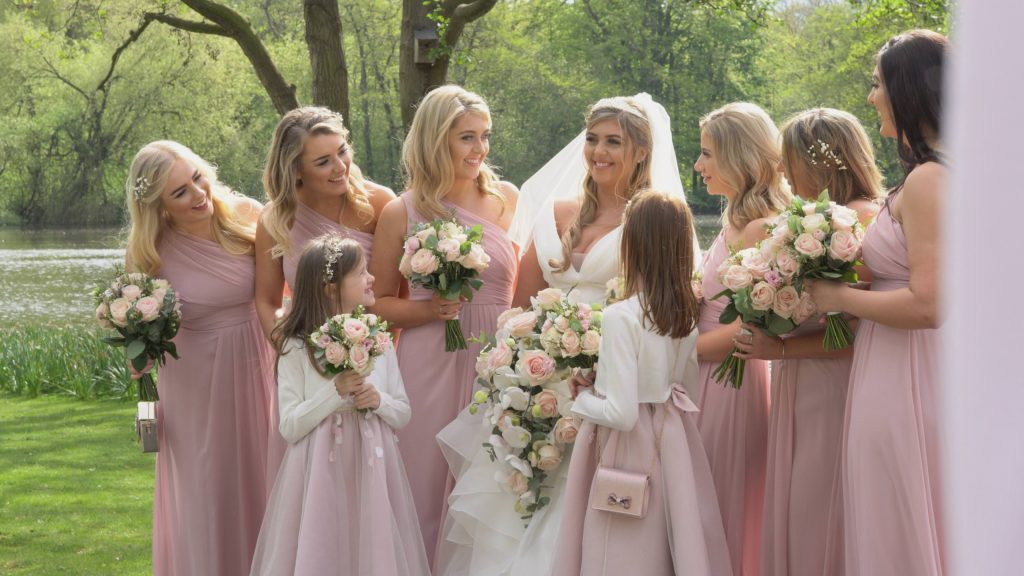 a still from the wedding videographer of the bride and her bridesmaids with blush pink floor length dresses and bouquets