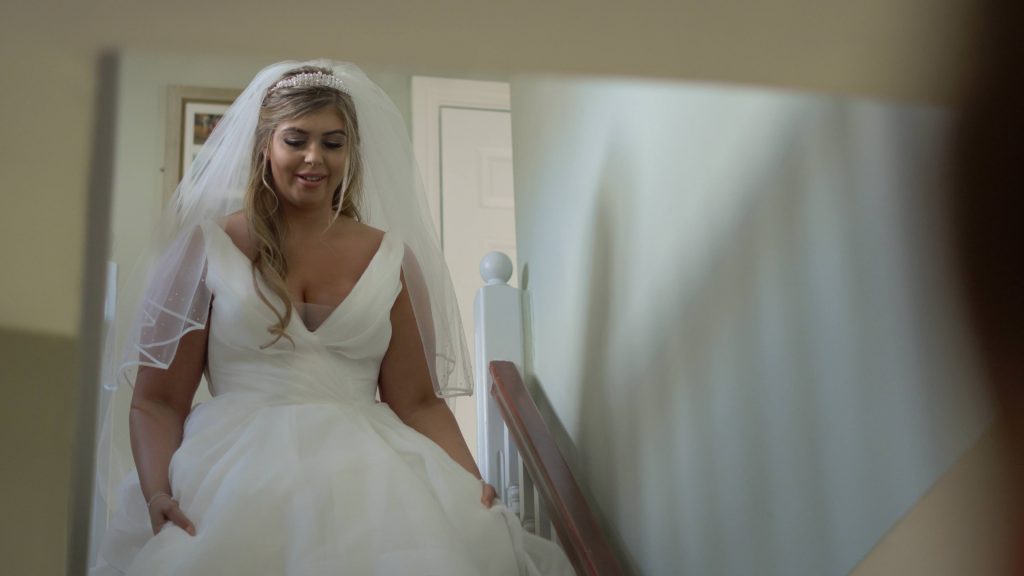 the bride smiles nervously as she walks down the stairs at her parents home in Oxton before she gets married 