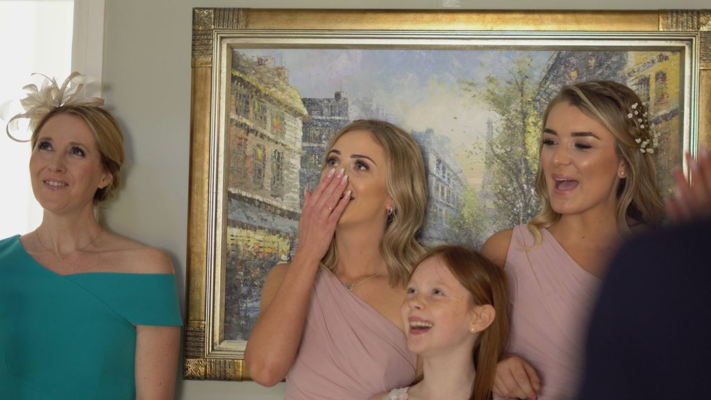 a still from the wedding video of the bridesmaids and friends reacting to the first look of seeing the bride before her wedding