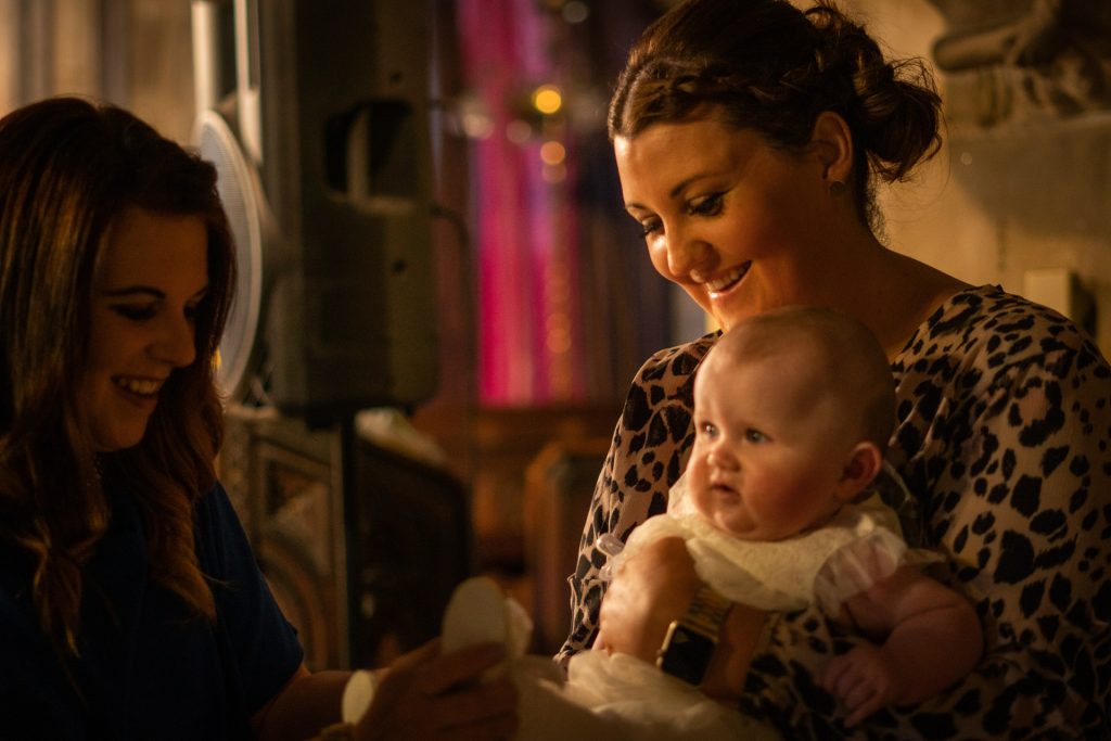 a documentary photographer captured this moment of a mum holding her baby girl soon to be christening in Lancashire laughing with her friends