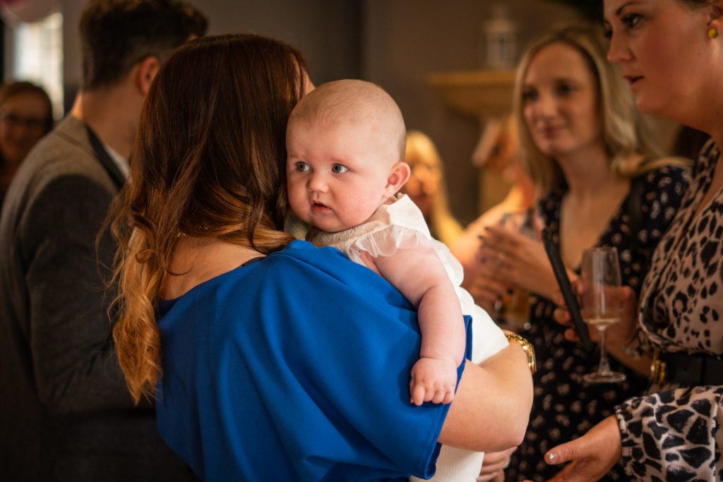 someone holds a little girl over there shoulder as she looks around the room during her christening party at Site Pizzeria