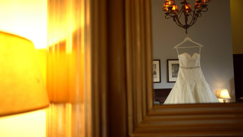a beautiful strapless lace wedding dress hangs from a chandelier in a suite at Peckforton Castle