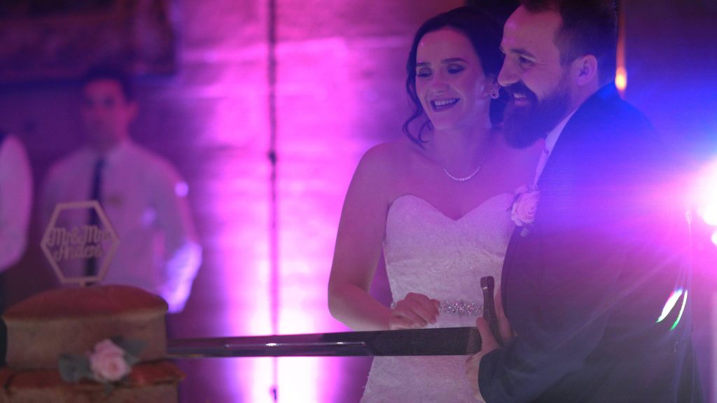 a bride and groom cute their unique wedding cake of pork and meat pies with a giant sword during their wedding evening at Peckforton castle