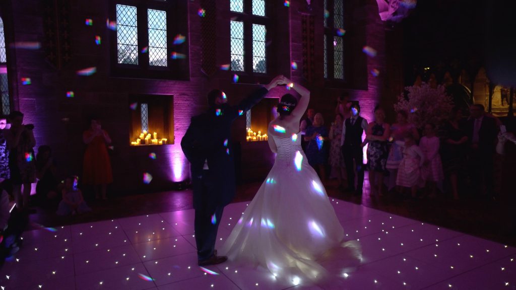 a wide shot of a bride and groom enjoying a spin during their first dance in the great hall at Peckforton Castle