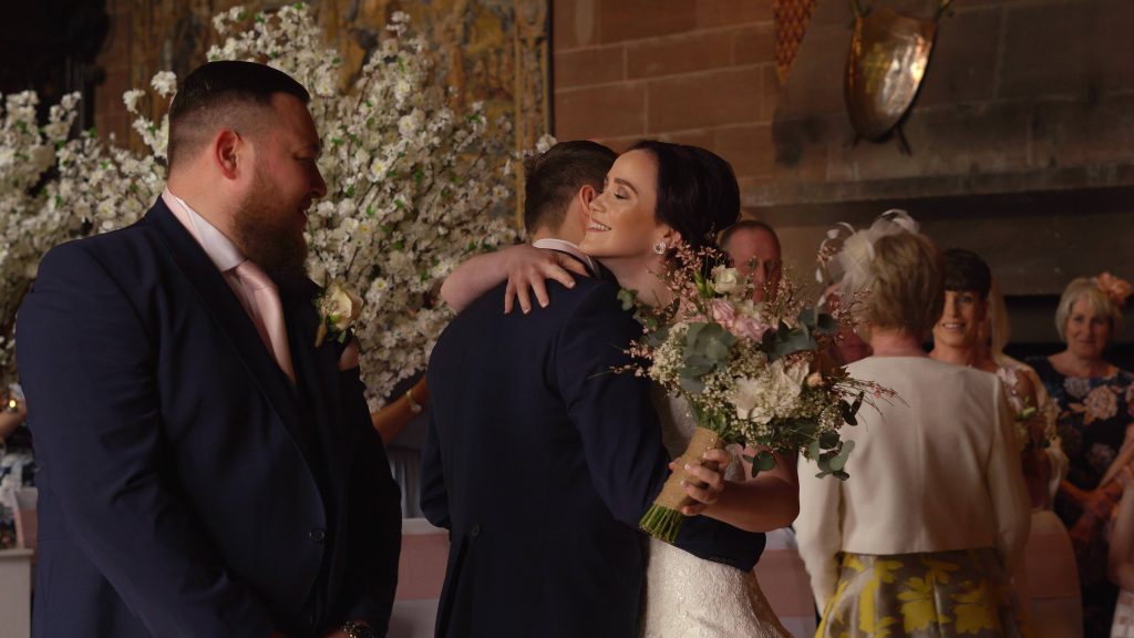 a still from the wedding video of a bride called Lisa giving her groom Ste a hug with her rustic bouquet during their peckforton castle wedding