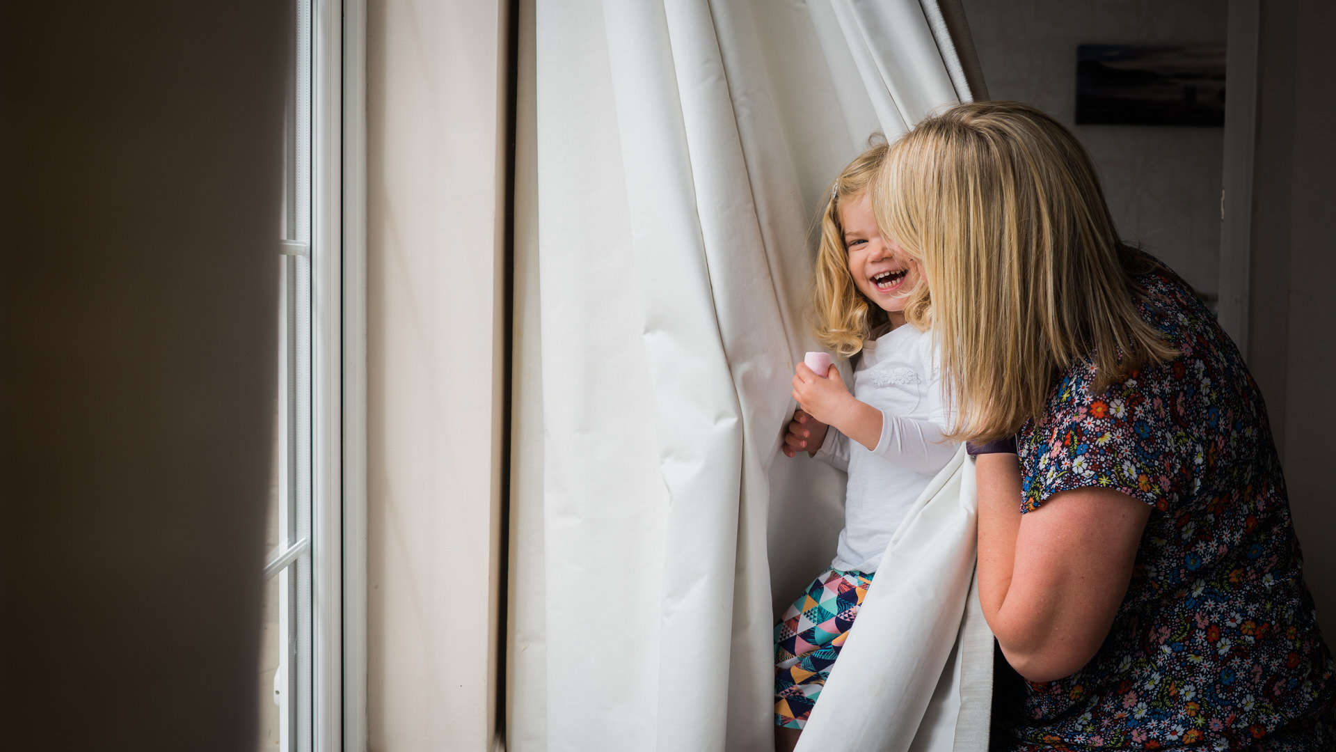 a natural photograph of girl playing peekaboo with her mum and photographer