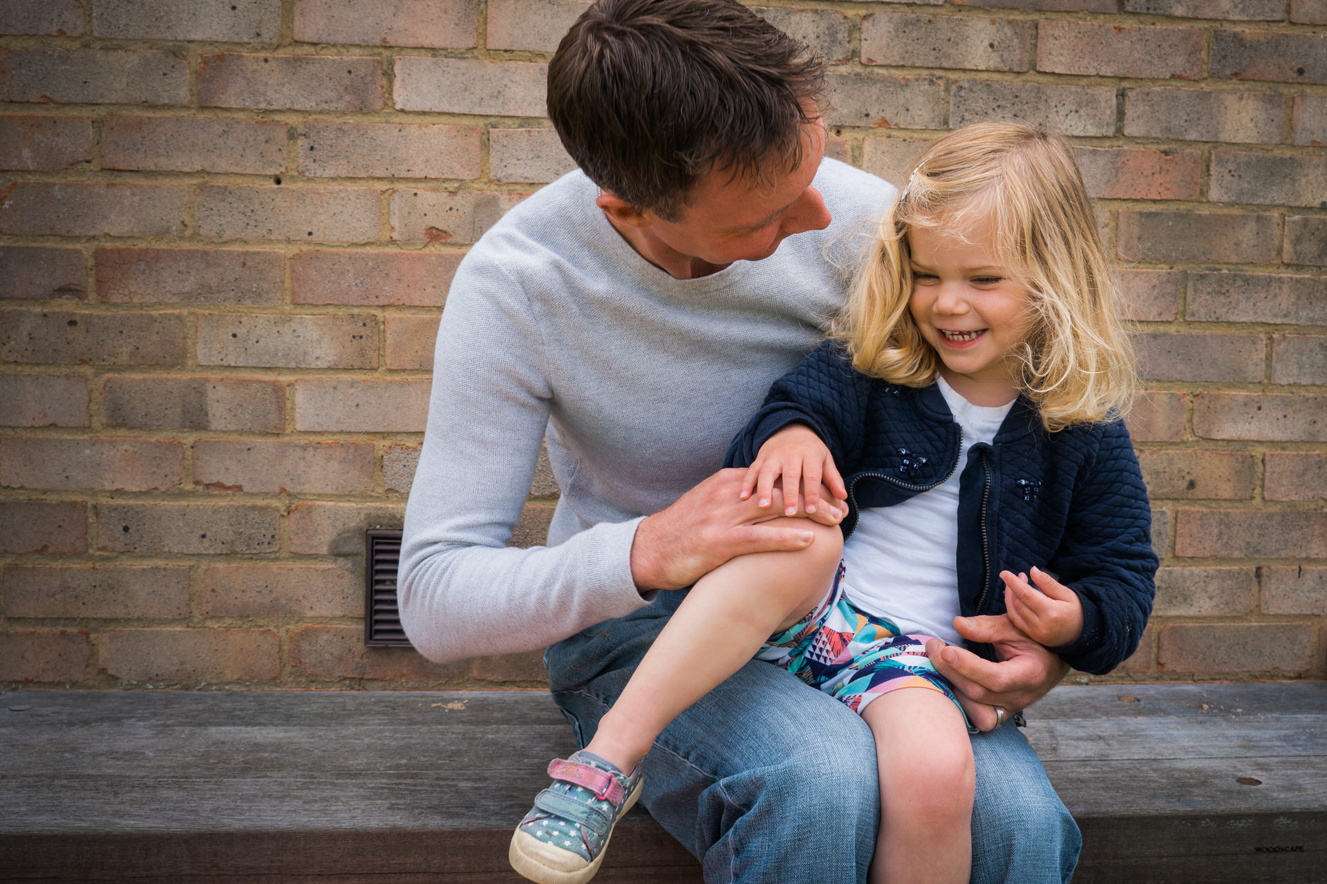 a little girl sits on her dads knee giggling during a relaxed family photo shoot by love gets sweeter