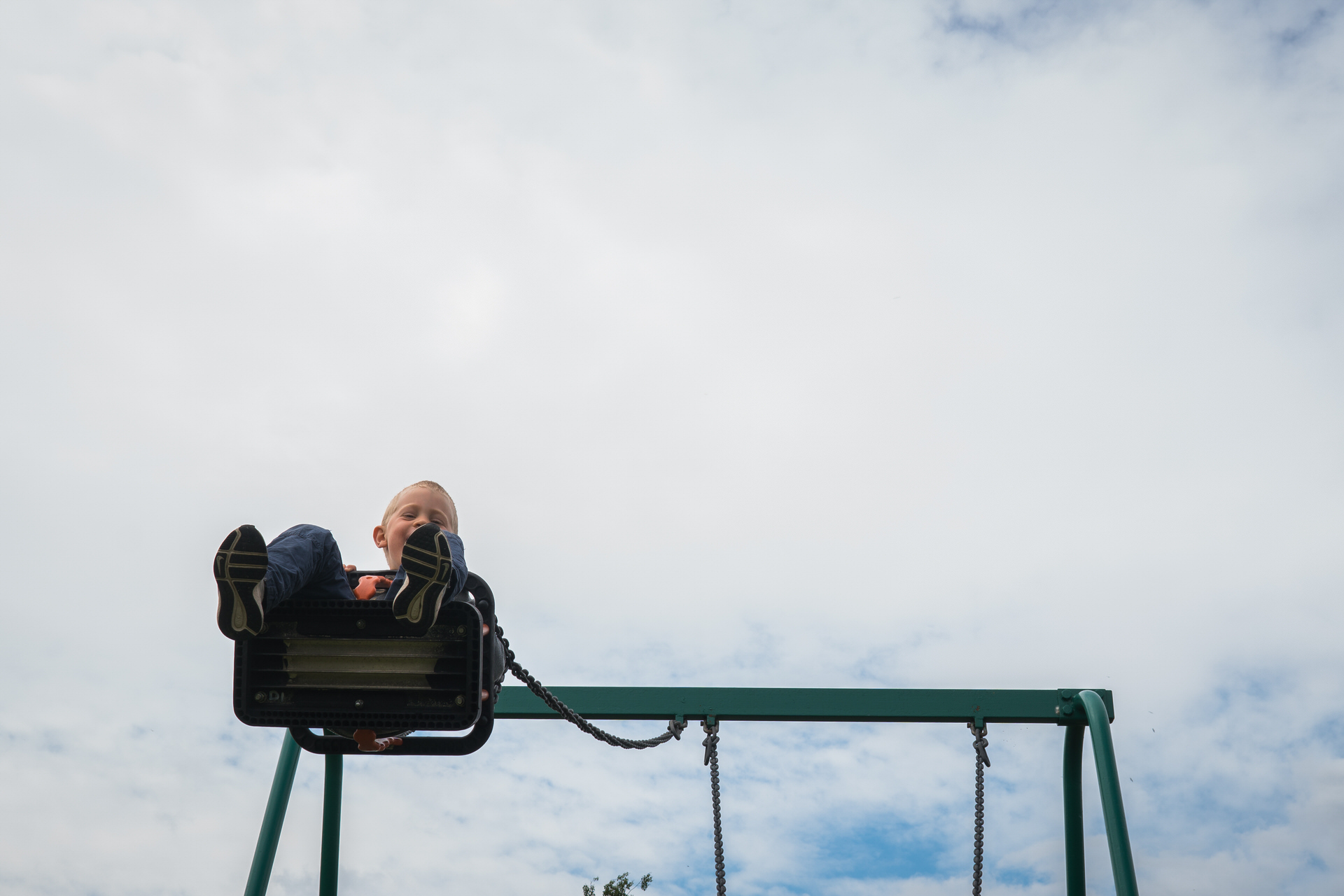 a photograph of a young boy swinging high up on the park swings during an outdoor family session photo shoot