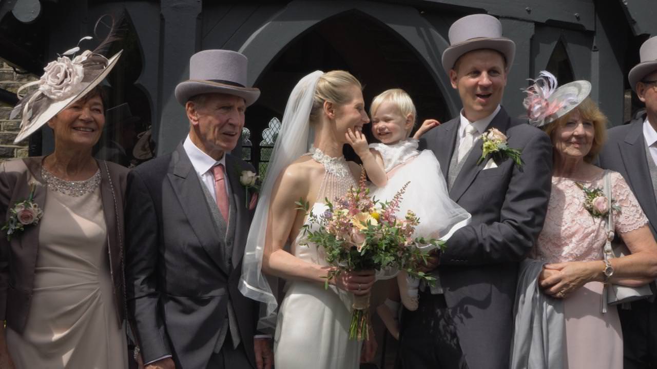 a flower girl reaches for her Mum's face during family wedding photos outside St Marks