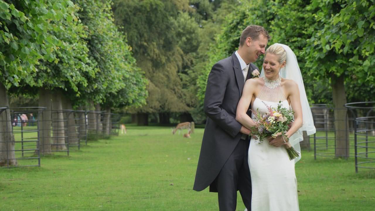 a bride laughs with her groom posing for the wedding video at Dunham Massey